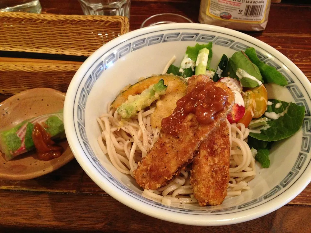 A cold bowl of Kyoto-style vegan soba topped with crispy plant-based tempura, a comforting and delicious dish